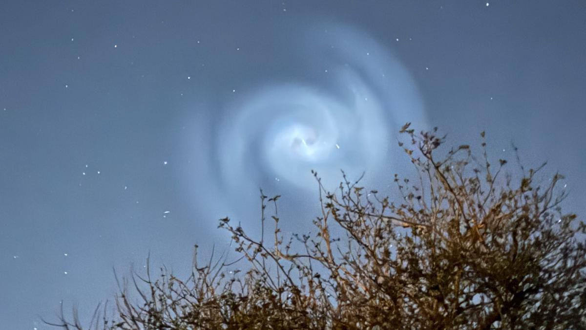 A spiral light in the sky seen over Heage in Derbyshire. The image also shows the top of a tree or bush from the bottom right of the frame