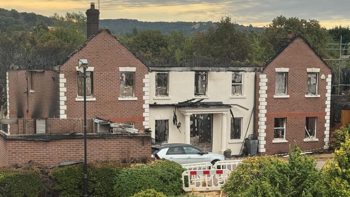 A large building with white pillars, significantly destroyed by fire. The roof has burnt away and much of the back of the building, as visible through the door and many windows.
