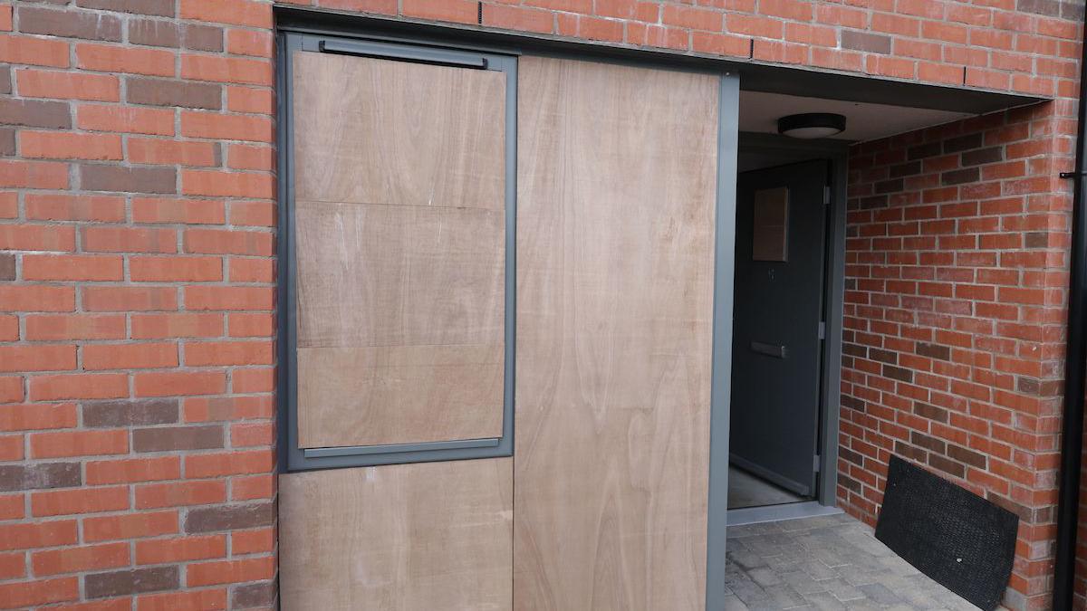 A close up of the entrance to a house with its windows boarded up in north Belfast following sectarian attacks on 21 May. The front door of the property is open and the building is made of new red brick.