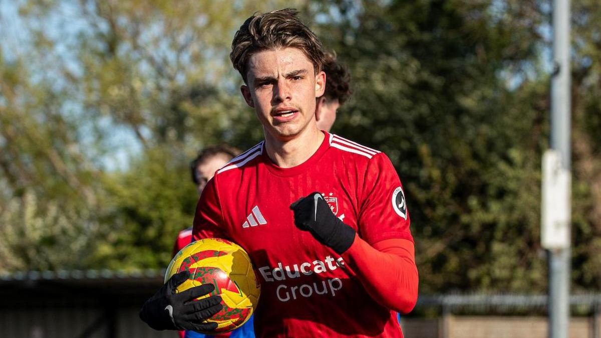 Callum West in gloves holds the ball while celebrating a goal