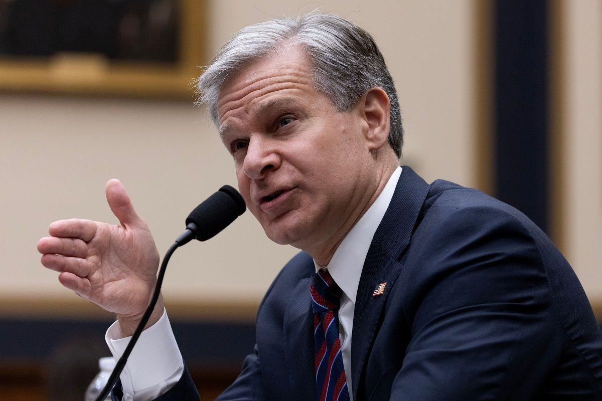 A grey-haired main in front of a microphone, gesturing with his hand