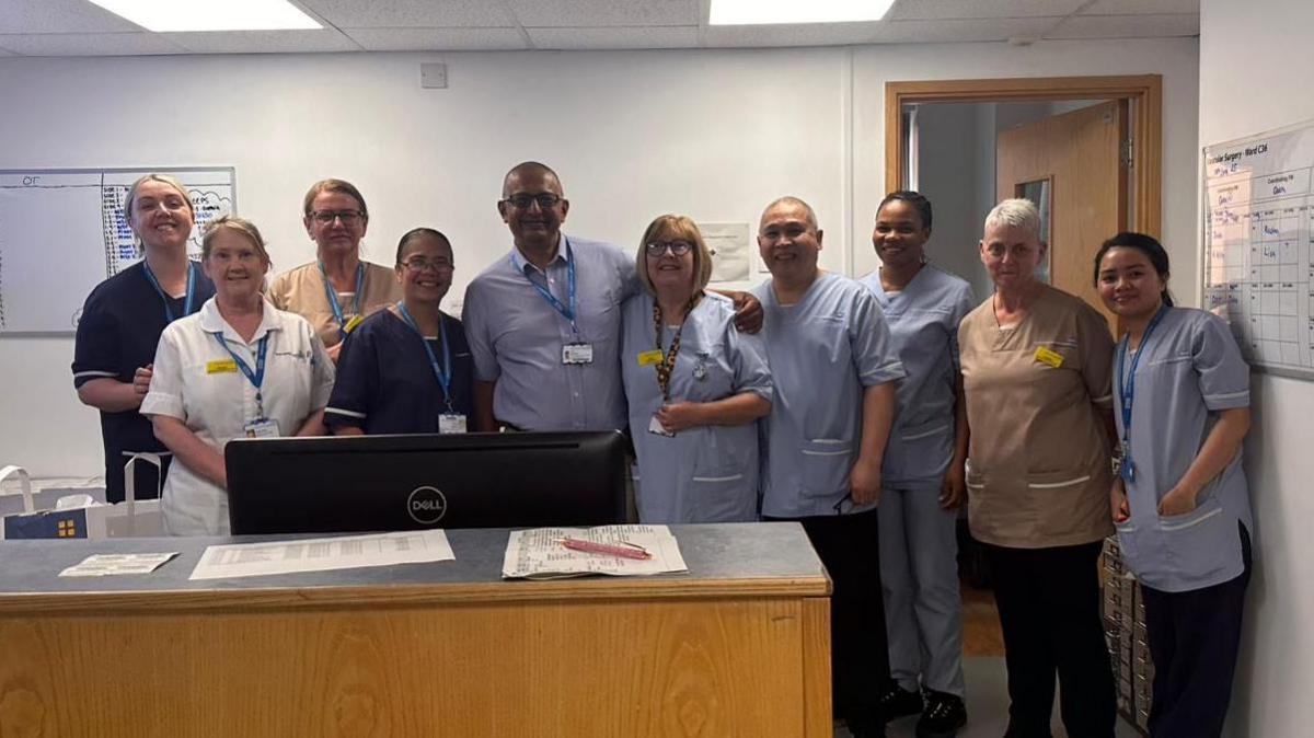 Ben Banerjee with nine of his hospital colleagues. They are standing in a reception area behind a wooden desk.