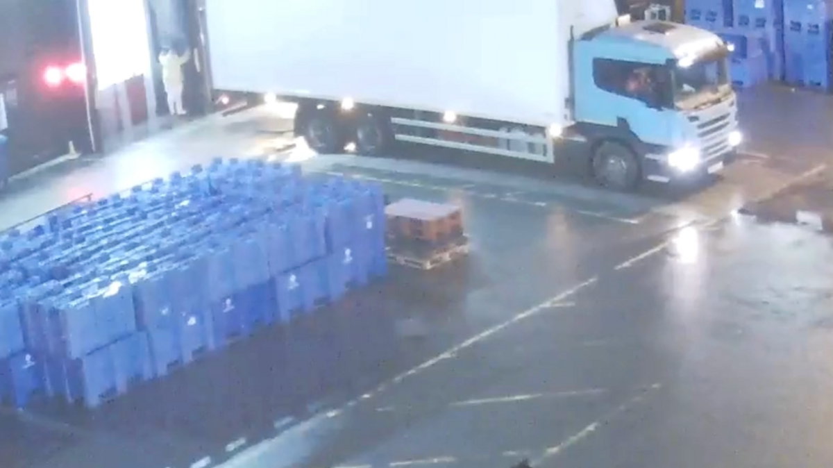 A stack of blue crates two high and a white lorry in a loading bay with a man in a white outfit at night.