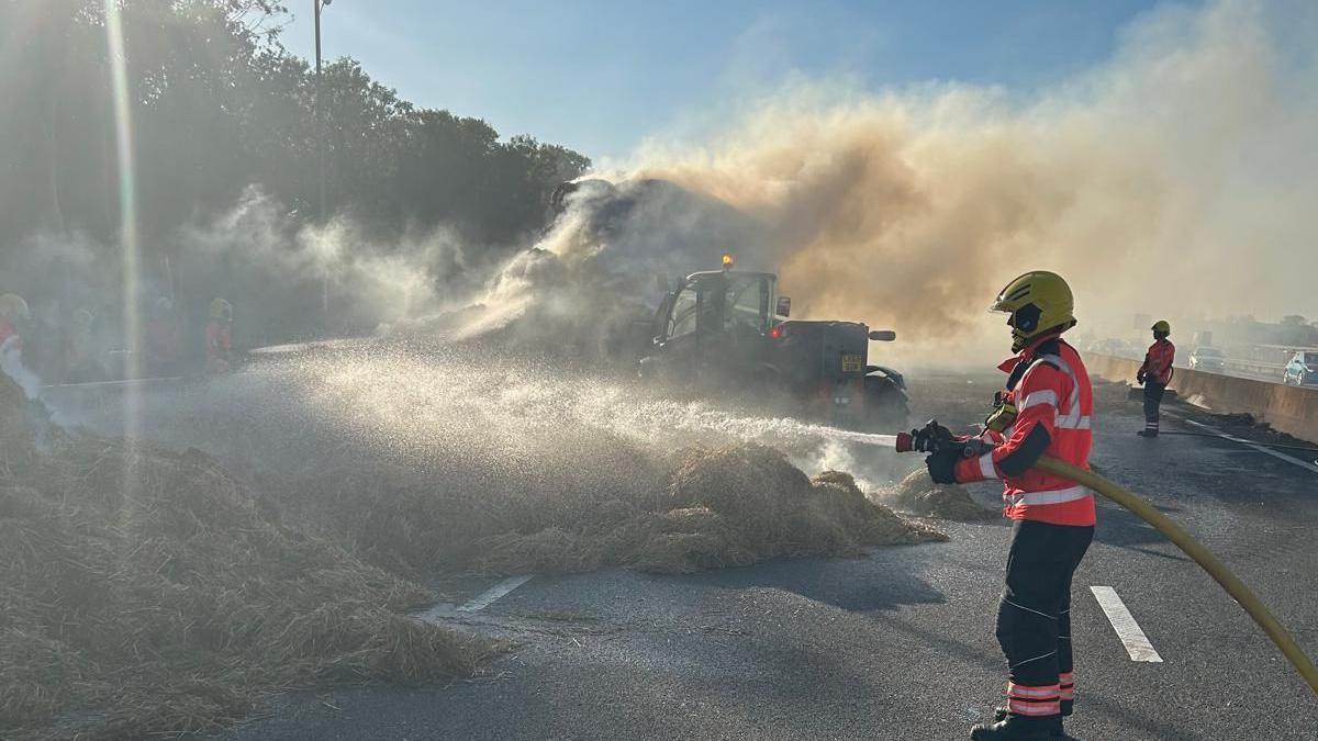 A firefighter is pointing a hose at a pile of material and a tractor engulfed in smoke