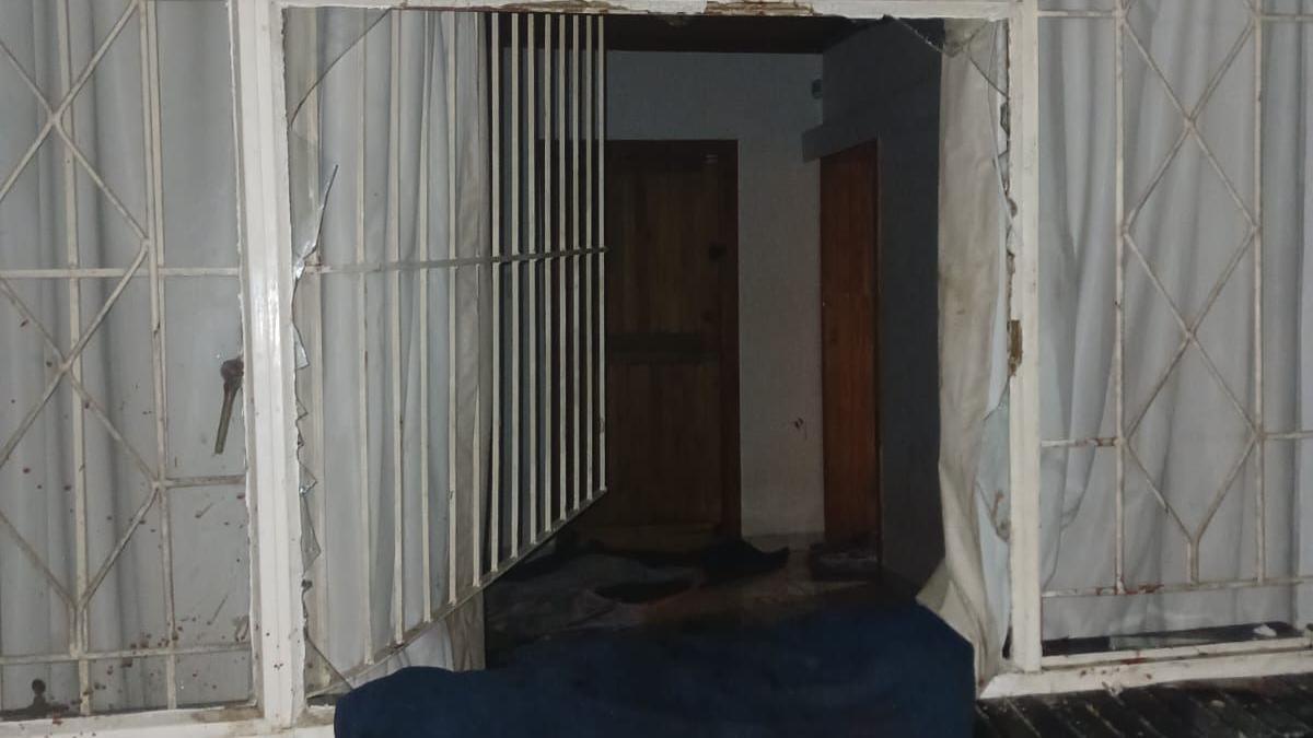 A broken window with some glass shards remaining in a picture taken outside a house in Johannesburg where Ethiopian nationals were found. The burglar bar has been forced open and a blue blanket covers the bottom part of the window, which provides a view into an unlit room.