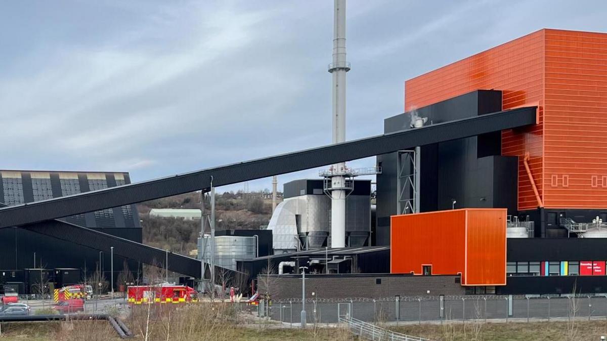 Large black and orange factory with a chimney and several pipes 