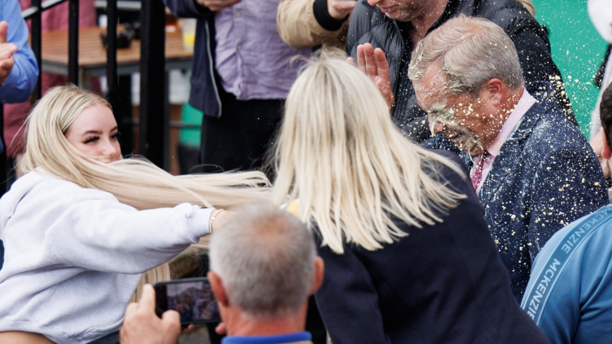 A blonde woman throws a milkshake over Nigel Farage, who at the time was the leader of Reform UK party and prospective parliamentary candidate for Clacton. His eyes are closed as the liquid splashes over his face and his mouth is closed in a grimace. 