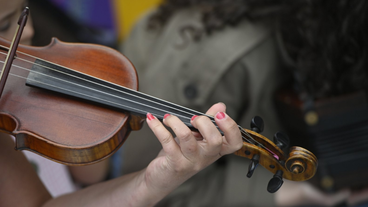 A brown violin being played during the All-Ireland Fleadh in Belfast. There is a hand with painted fingernails at the end of it.