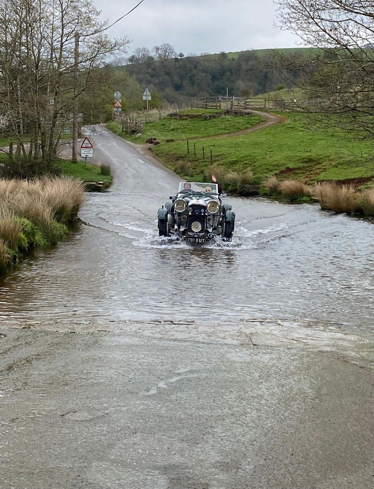 An old motor car passes through a flooded road