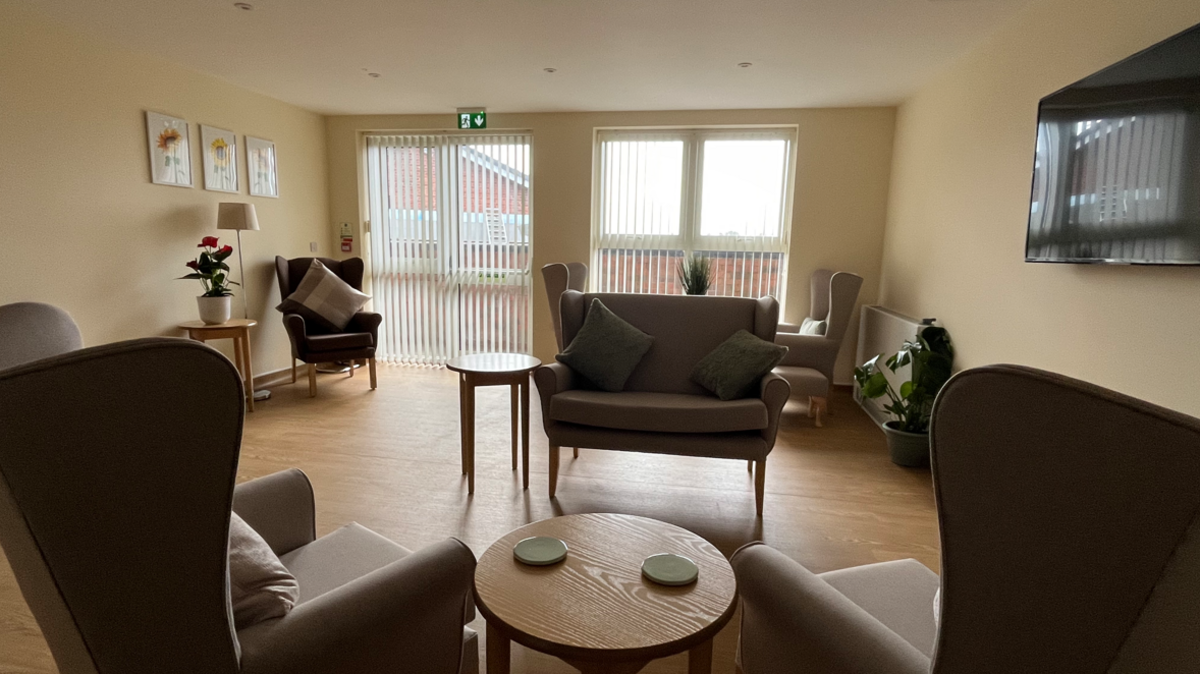 A room with six xhairs on a wooden floor with windows with blinds on the far wall and flowers on a low table