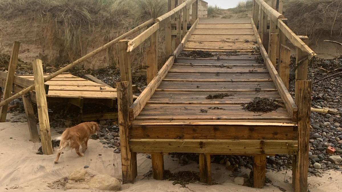 A damaged walkway onto the beach with one section broken and lying on one side 