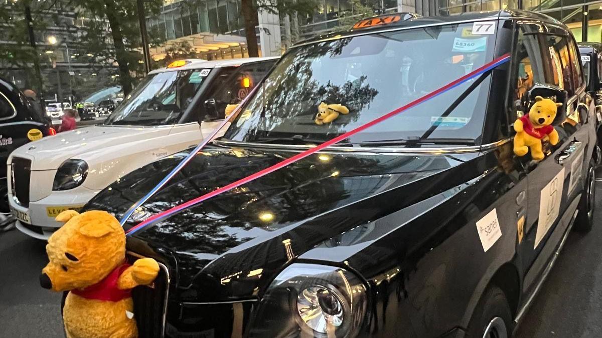 Black cab with a Winnie the Pooh soft toy attached to the front with red and blue ribbons to the front windscreen.