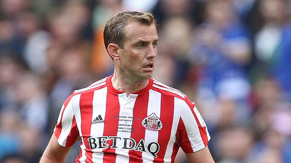 Lee Cattermole looking up with the ball down below at his feet in a red-and-white Sunderland kit