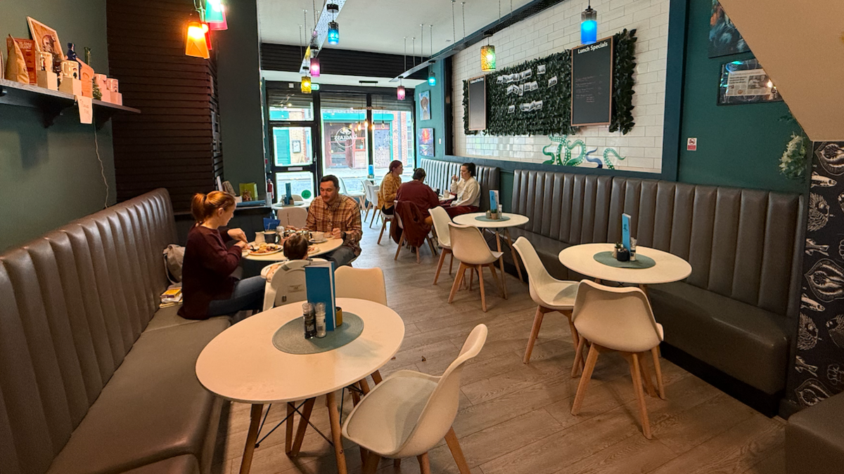 An internal view of the SeaGlass Cafe. Customers sit around round, white tables enjoying meals. There are brown leather-look banquette seats along the walls and a wooden floor.