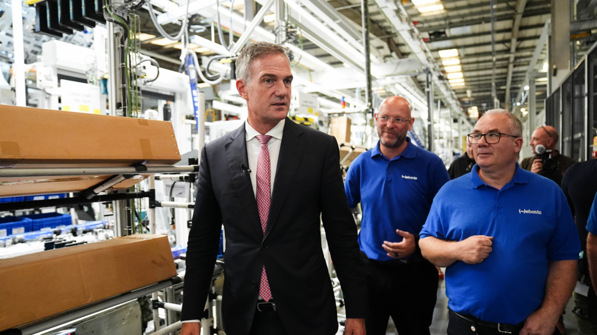 Secretary of State for Business and Trade Peter Kyle MP during a visit to Jaguar Land Rover supplier, Webasto - he is wearing a suit, walking past what appears to be high-tech machinery, with two workers wearing blue branded polo shirts walking next to him