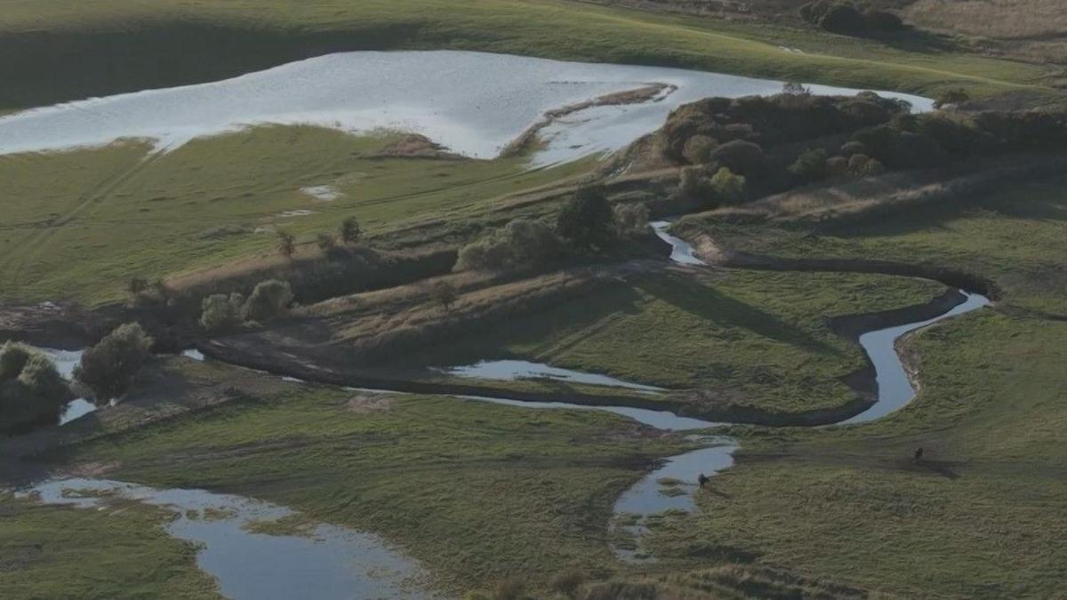 A river in a green fields, which swirls off course into more green fields in a bendy shape.