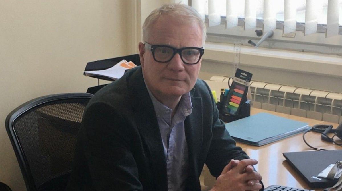 West Midlands Mayor Richard Parker with his hands clasped together, wearing glasses facing the camera. He is sitting at a desk and paper and trays are behind him.