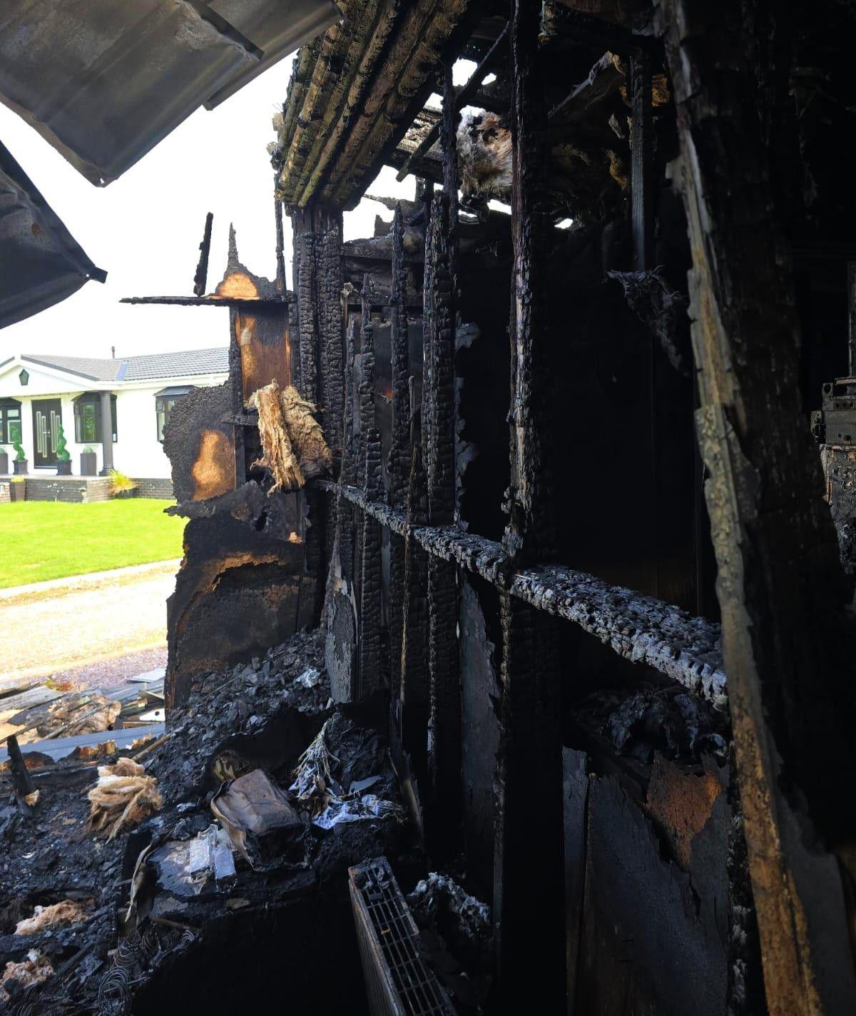 The badly burned exterior of a holiday home, with an intact bungalow-style white holiday home in the background