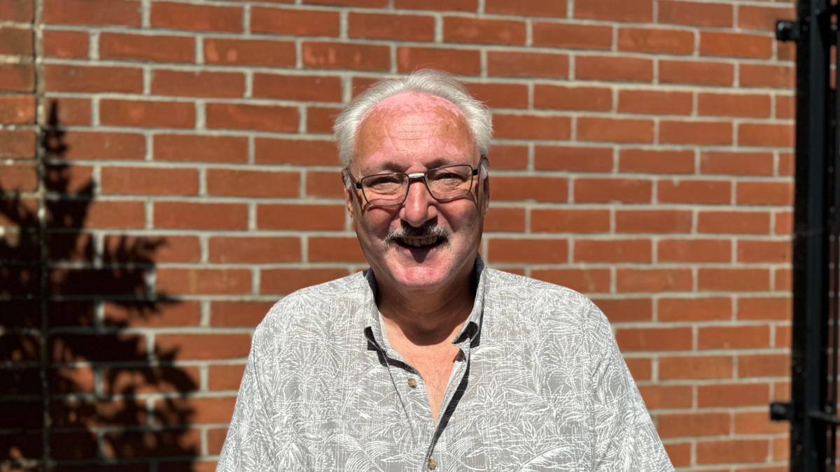 A man in a shirt smiling while standing in front of a brick wall