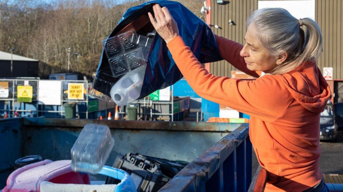 Stock image of a woman emptying recycling into a skip