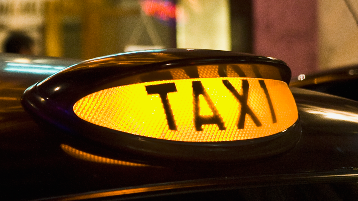 A yellow taxi sign on the top of a black cab