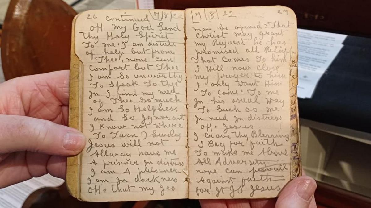 Hands are holding a small diary. The entries are written with a pencil.