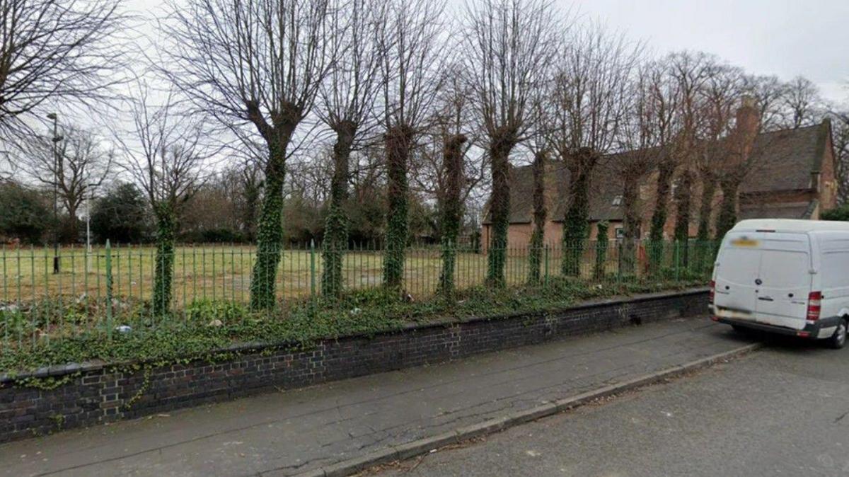 A general street view of an old bowling green in Derby, behind a green metal fence.