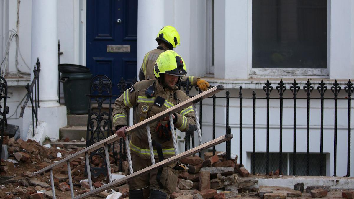 A firefighter holds a ladder in front of a property with rubble on the floor.