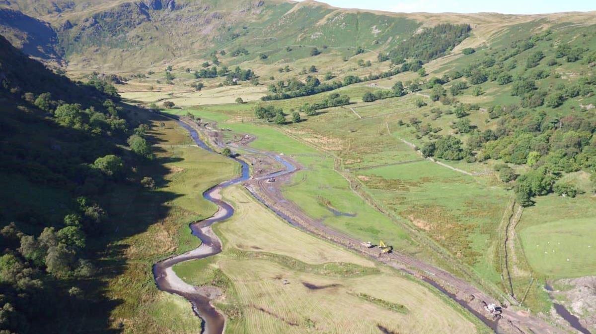 An aerial view of two streams of water down a rural valley. Diggers are working on one stream, the other meanders through the fields.