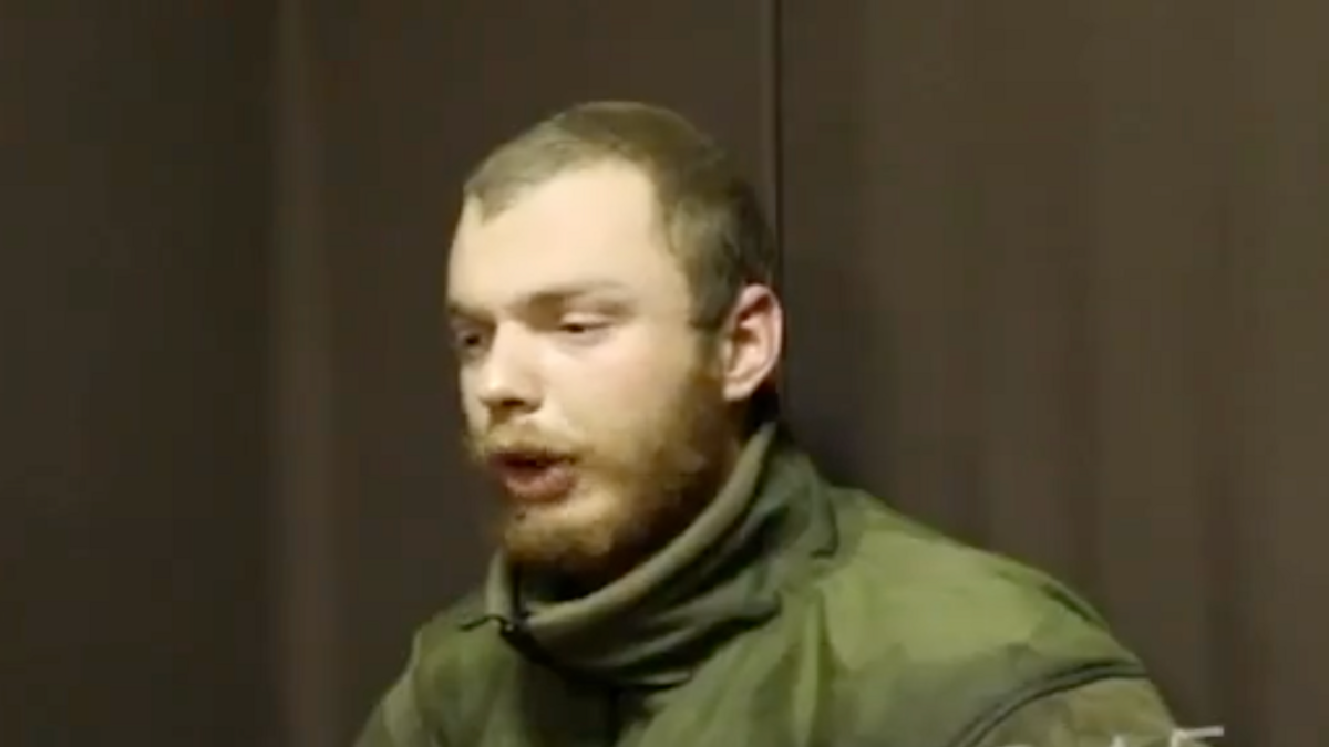 A man believed to be James Scott Rhys Anderson, 22, a former British Army soldier captured while fighting for Ukraine, is seen wearing green military clothing and sat in front of a plain brown background.