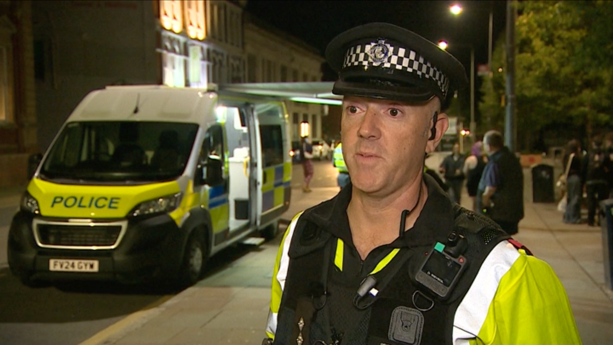 A policeman in a high visibility yellow jacket on a city centre street at night, with a police van behind him.