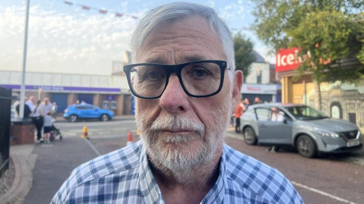 John MacVicar, in checked shirt, with grey hair and black rimmed glasses.