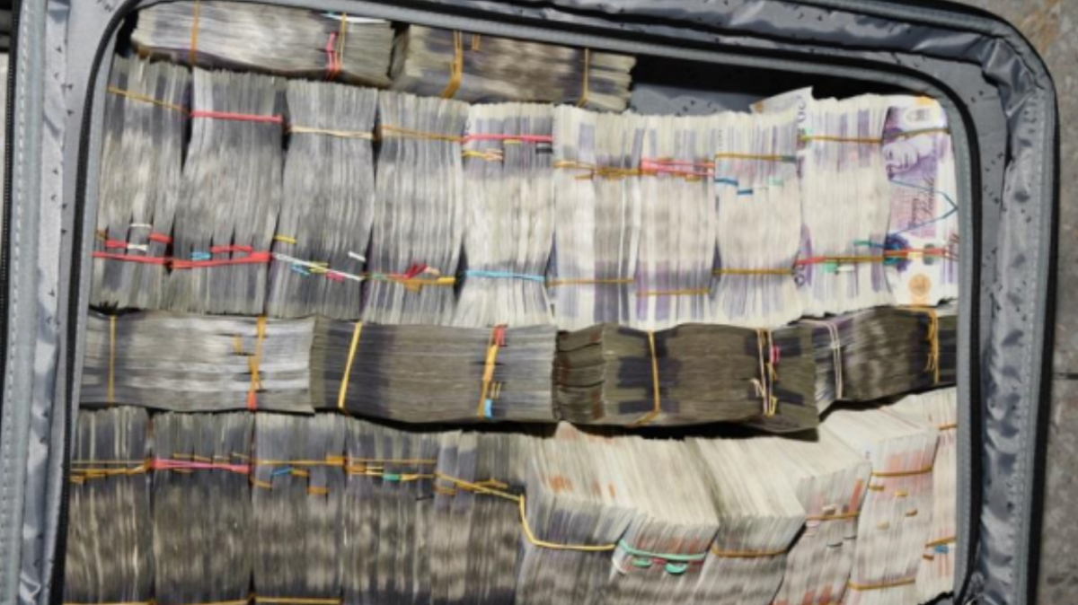 A suitcase filled with tightly packed bundles of of sterling banknotes, secured with rubber bands. The notes are arranged neatly inside the open suitcase