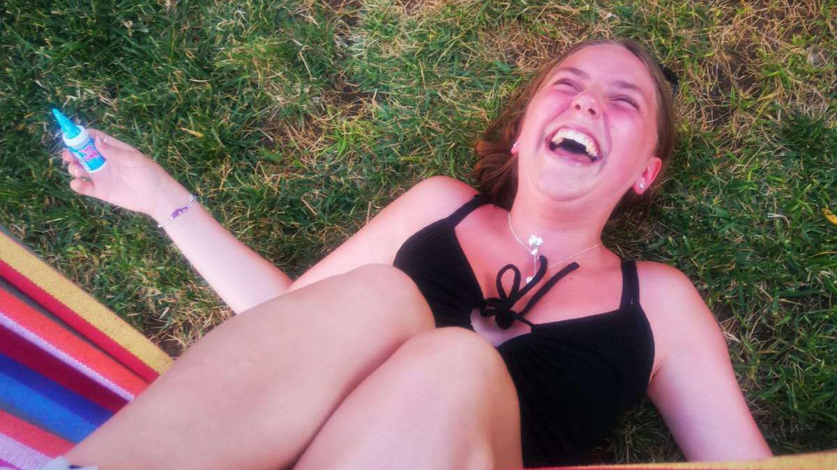 Chloe laughs while lying on green grass, she is wearing a black top and silver necklace. 