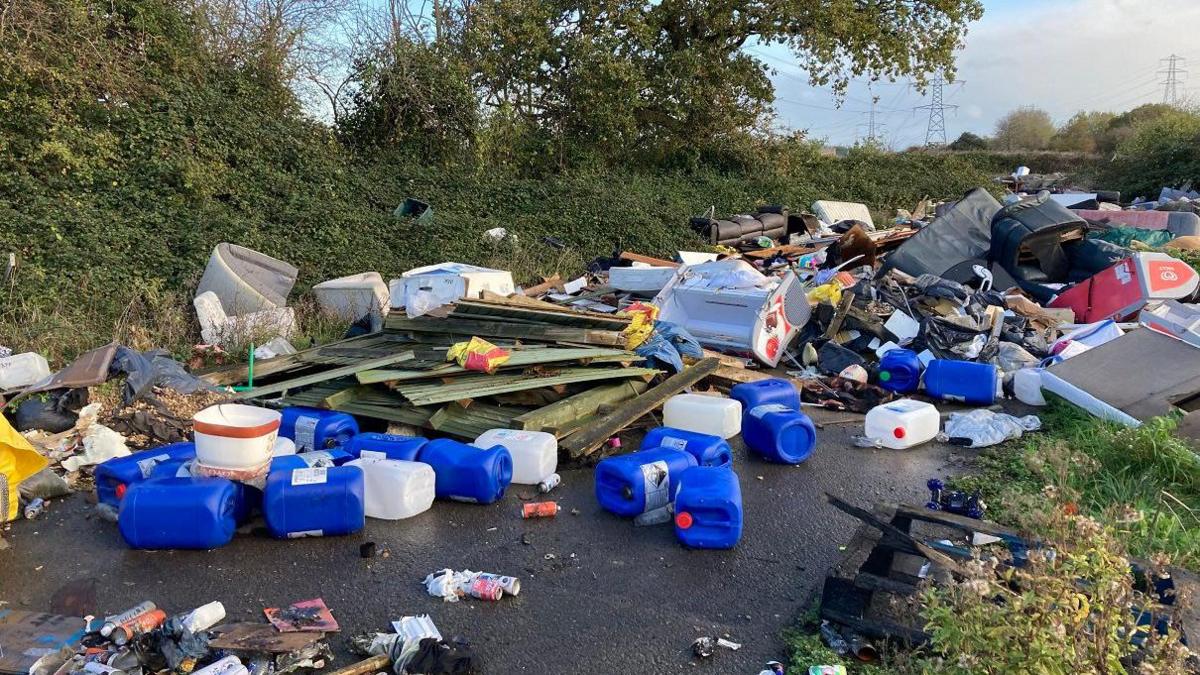 Rubbish dumped on a lane in Bristol. The image shows a variety of discarded items such as large plastic bottles, piles of wood and furniture.