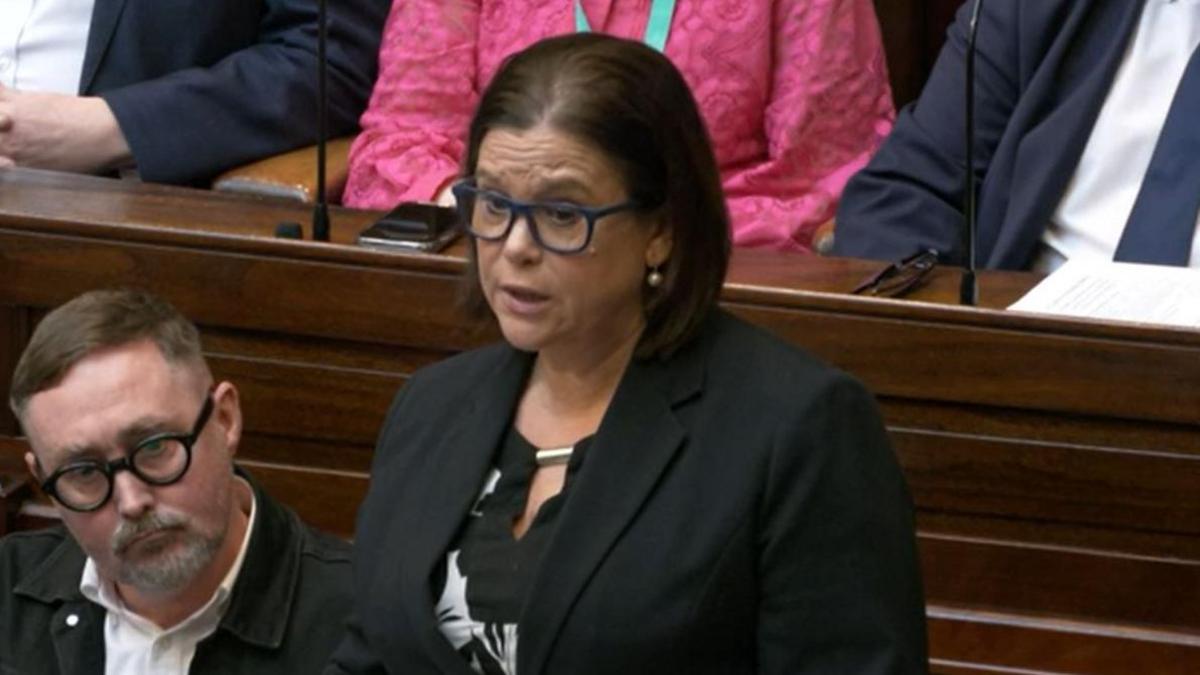 A woman speaking in the chamber wearing a black top and black blazer