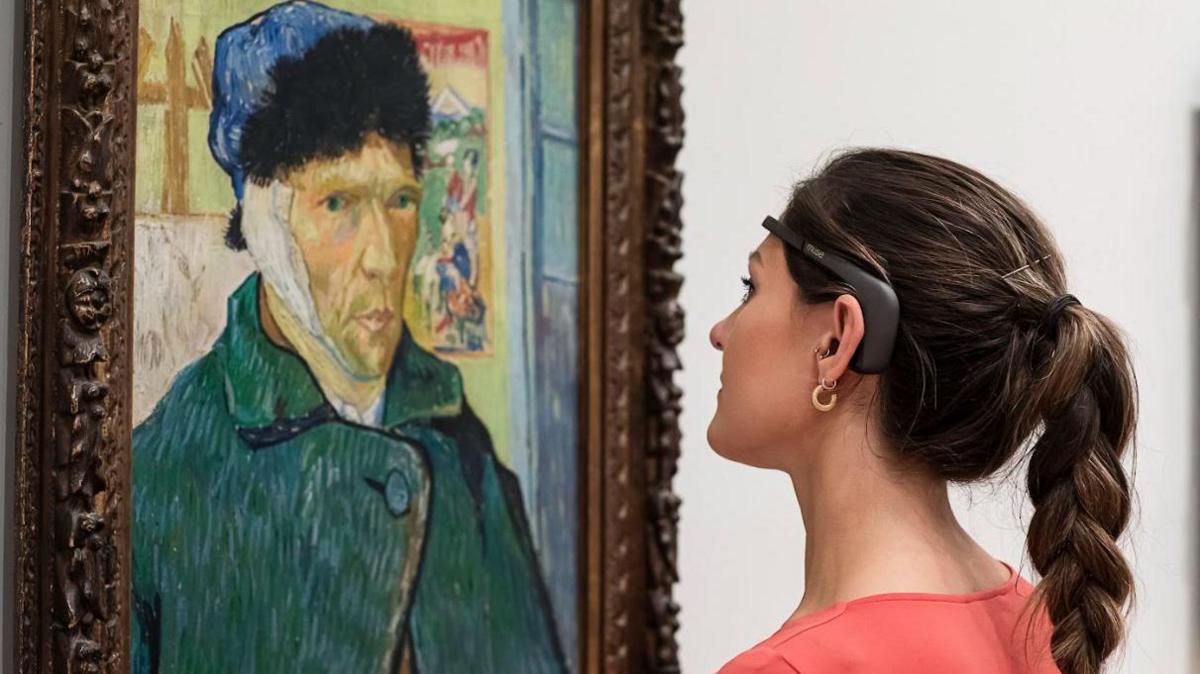 A woman looks at a picture of Vincent Van Gough with a headset on