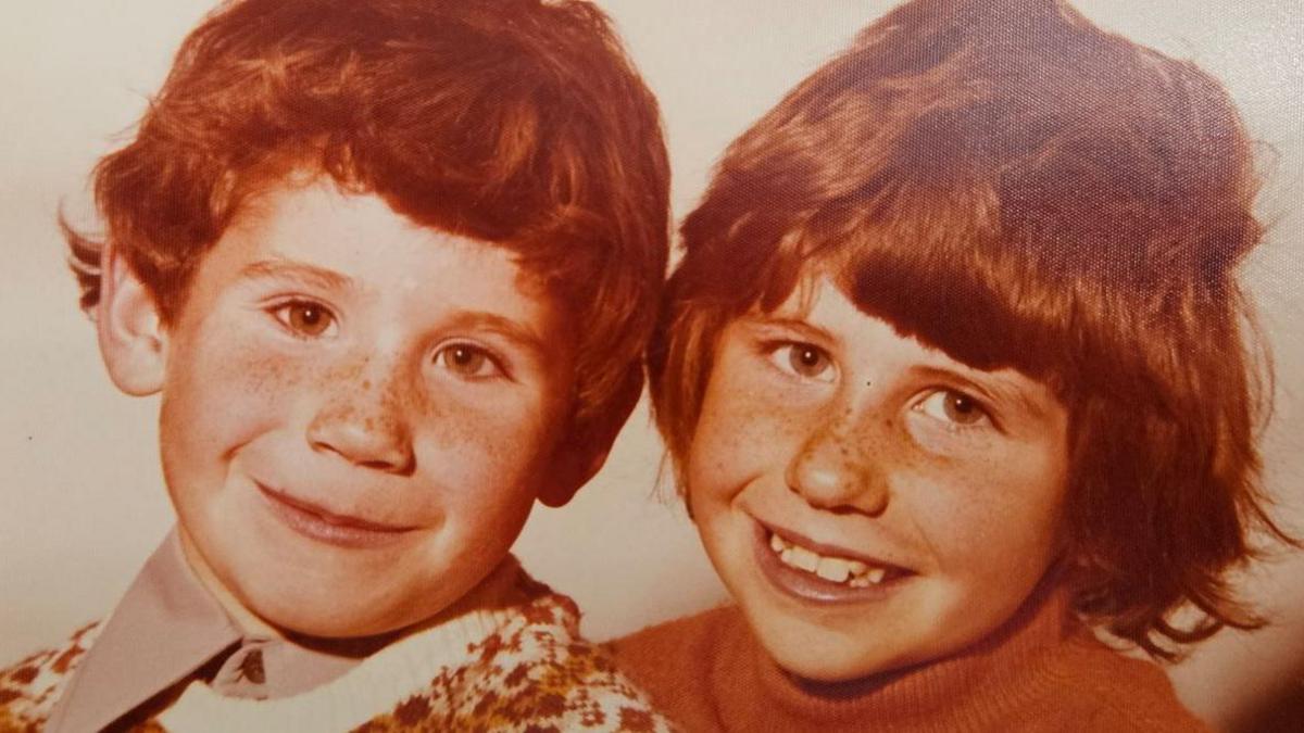 Old photo of Colin and Jenny as children. Both have woollen jumpers on and red hair and freckles