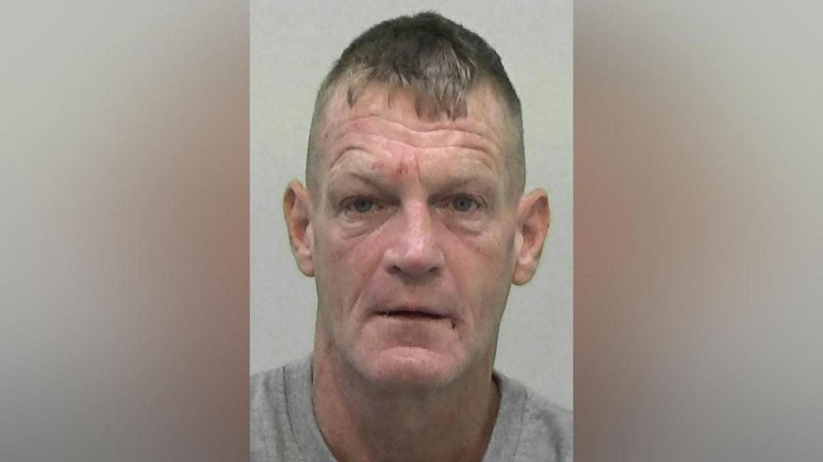 Mugshot of Stephen Thompson. He is clean shaven with short fair hair and deep wrinkles. He has a few marks on his face that look like small but recent wounds.