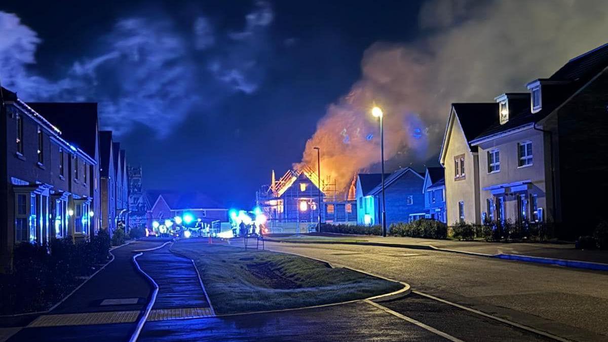 Homes being built on a new housing estate well alight with red flames, smoke and embers glowing against a night sky.