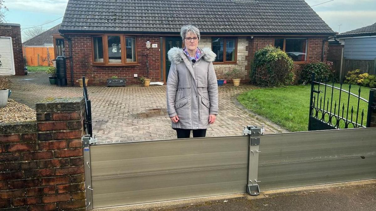 Elaine Merrick-Reed stands behind the flood barrier across her driveway