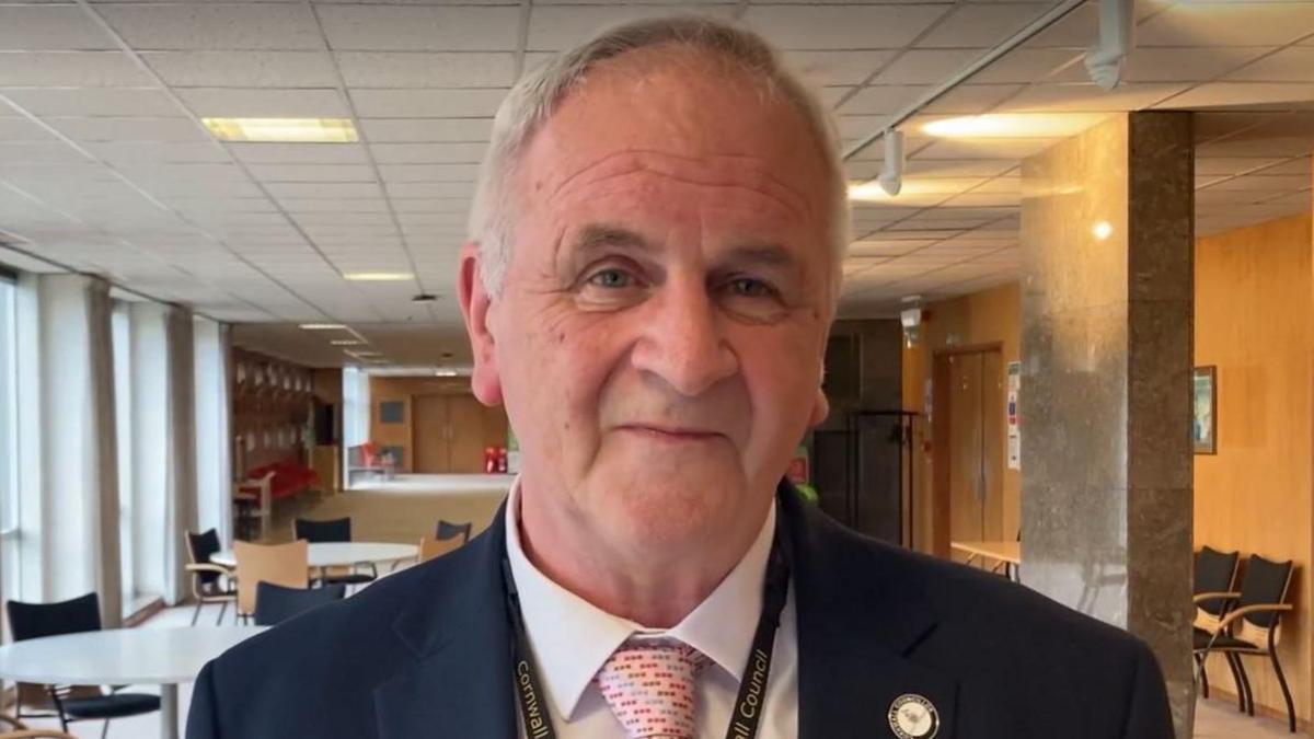 This is a close up photo of the new Reform leader in Cornwall. Cllr Paul Ashton is looking straight at the camera. He is smiling and wearing a tie, white shirt and a navy blazer. He has a lanyard around his neck, and there is a round, enamel badge on his blazer.