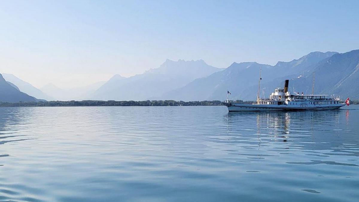 Lake Geneva surrounded by mountains. A boat on the right of the pic has a Switzerland flag. 