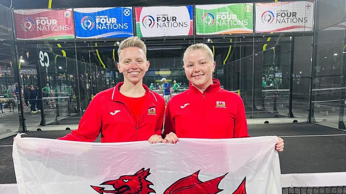Alex Oelmann and Molly Walsh on a padel court holding a Wales flag