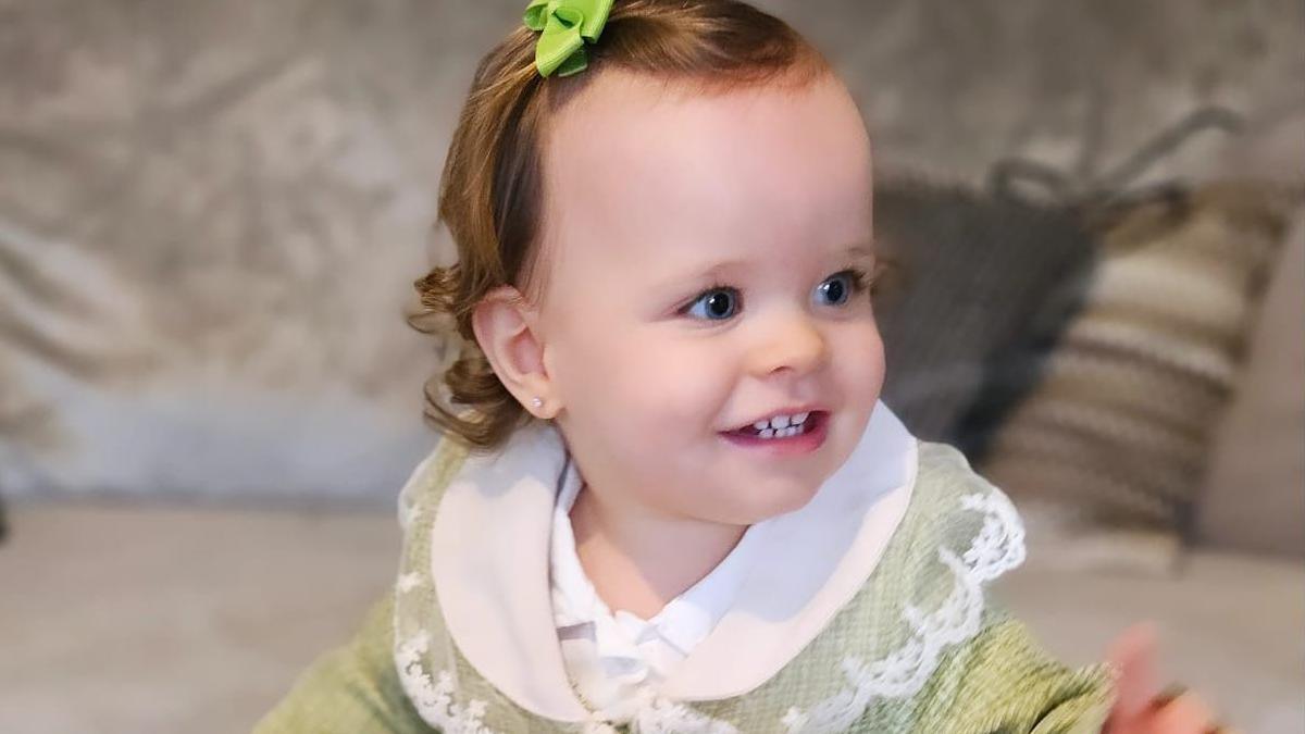 Sienna-Rose looks off to the side of the camera and smiles. She wears a green dress with a whilte collar and has a green bow in her hair