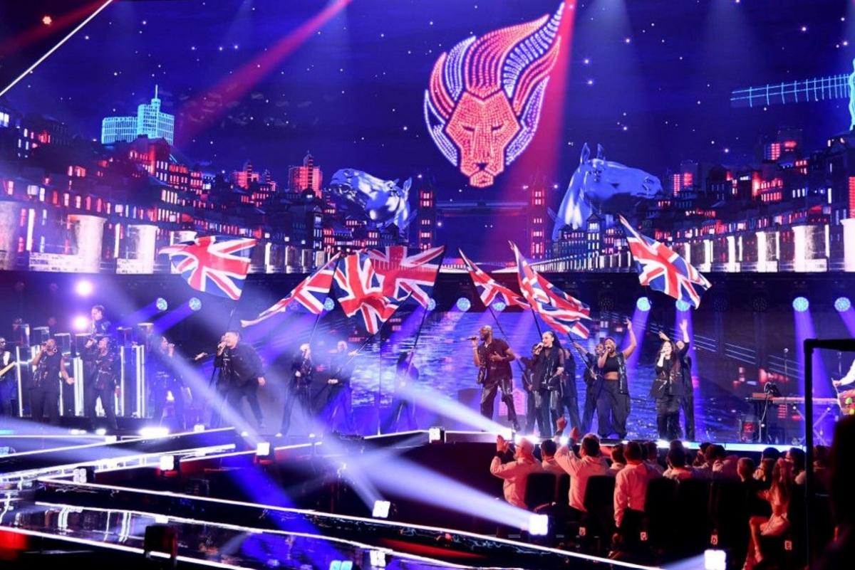 Flag bearers and flags were on stage, with skyline images in the background and people watching in the foreground 