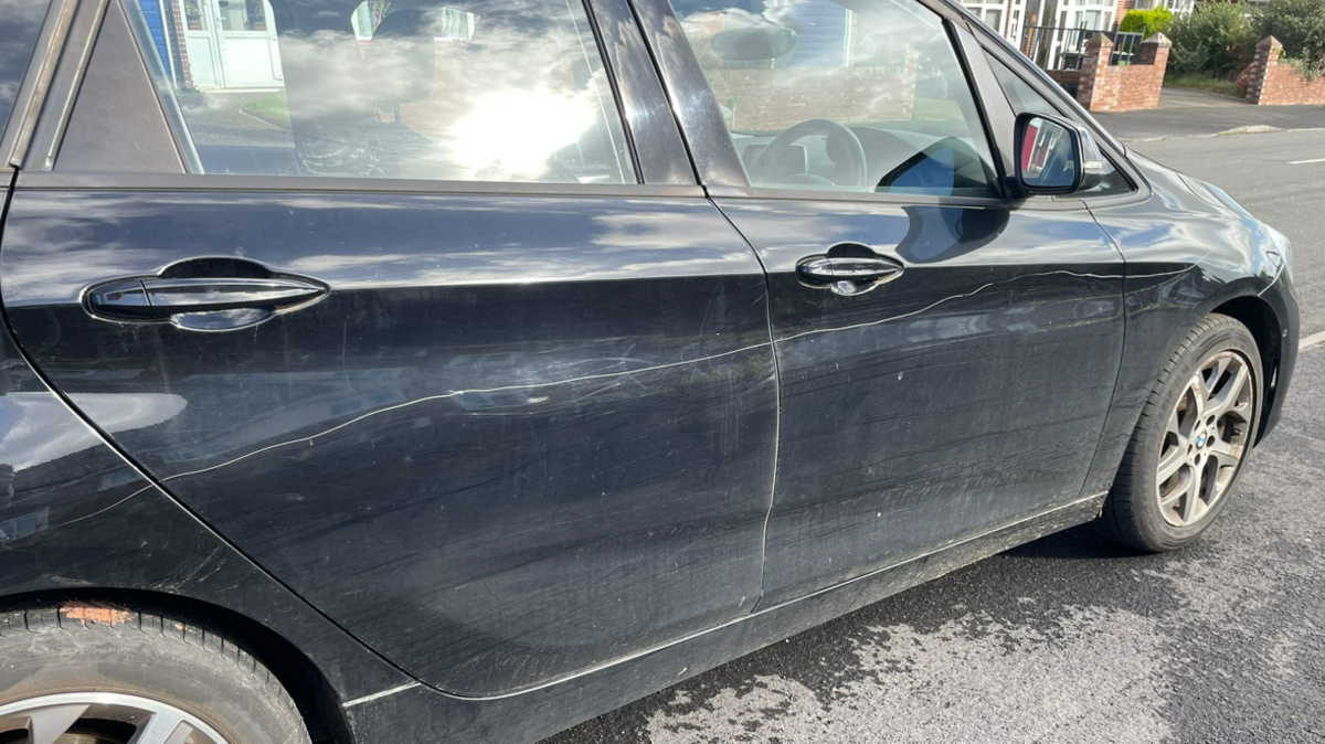 A navy blue car which appears to have been keyed along its driver side doors while parked on a road in Exeter.