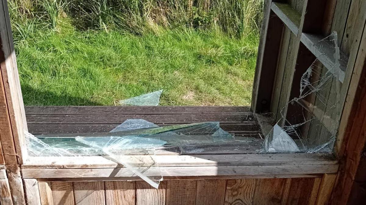 Glass from a window pane has been smashed and is lying on the edge of a brown wooden hide. 