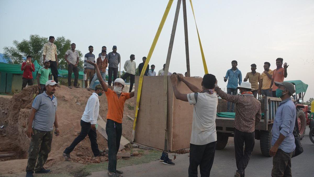 A crane was used to transport the wooden box containing the skeleton to its present site. The image shows men engaged in transporting the skeleton, surrounded by onlookers.