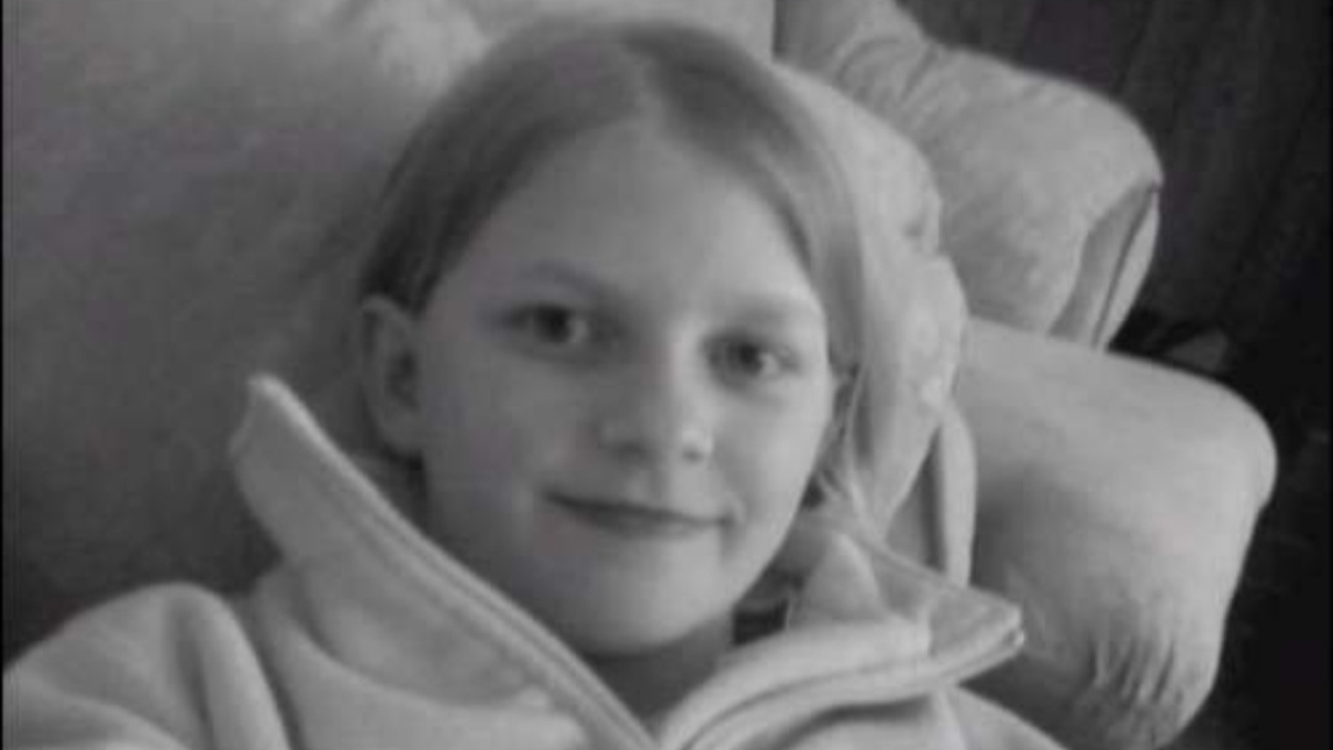 A black and white photo of a close-up of Sasha, lying back in an armchair, smiling to camera